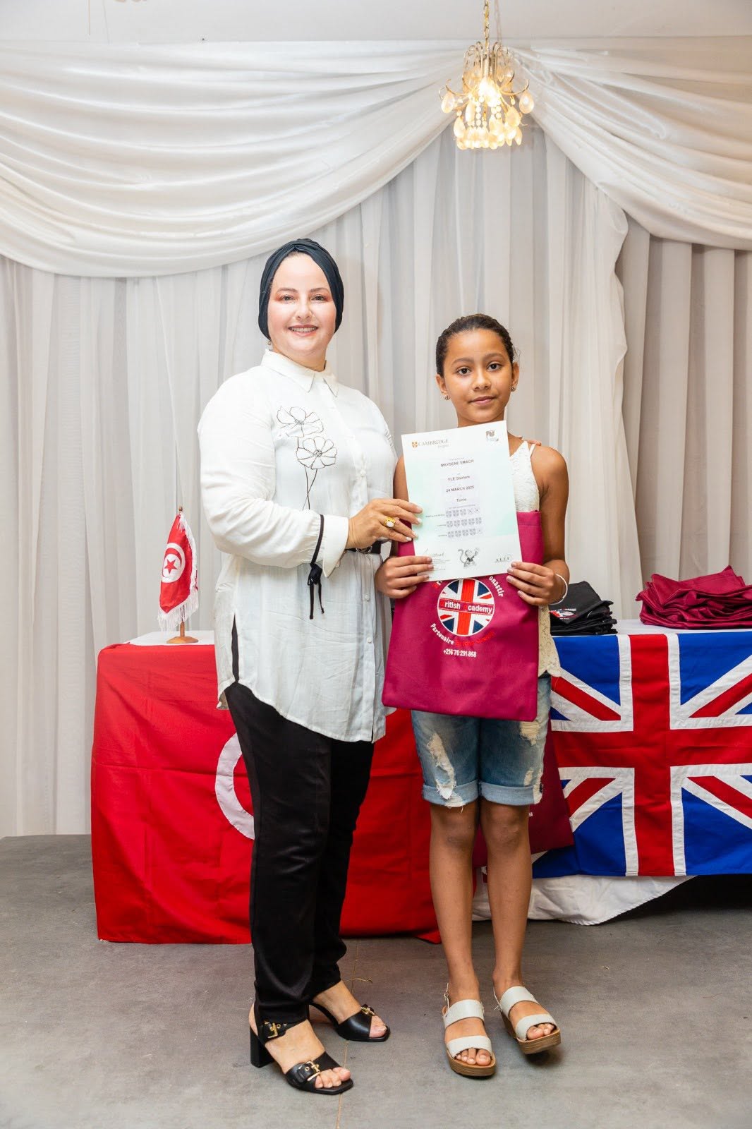 Student holding her Cambridge English YLE certificate with her teacher