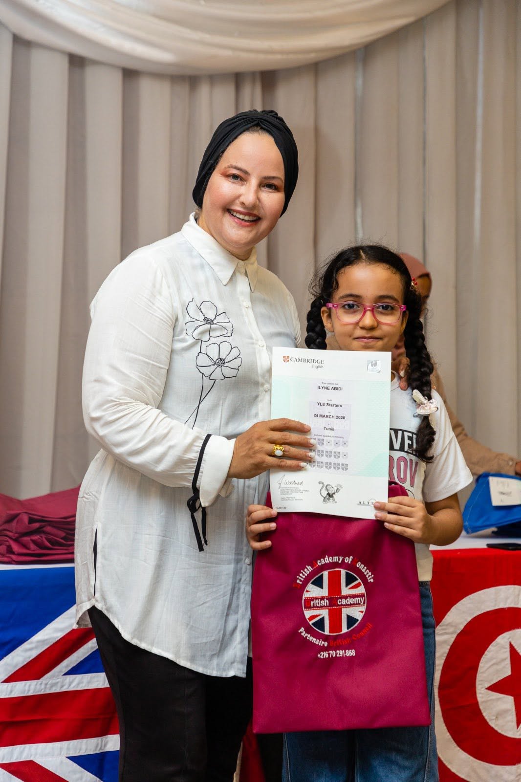Young student holding her Cambridge English YLE certificate with her teacher