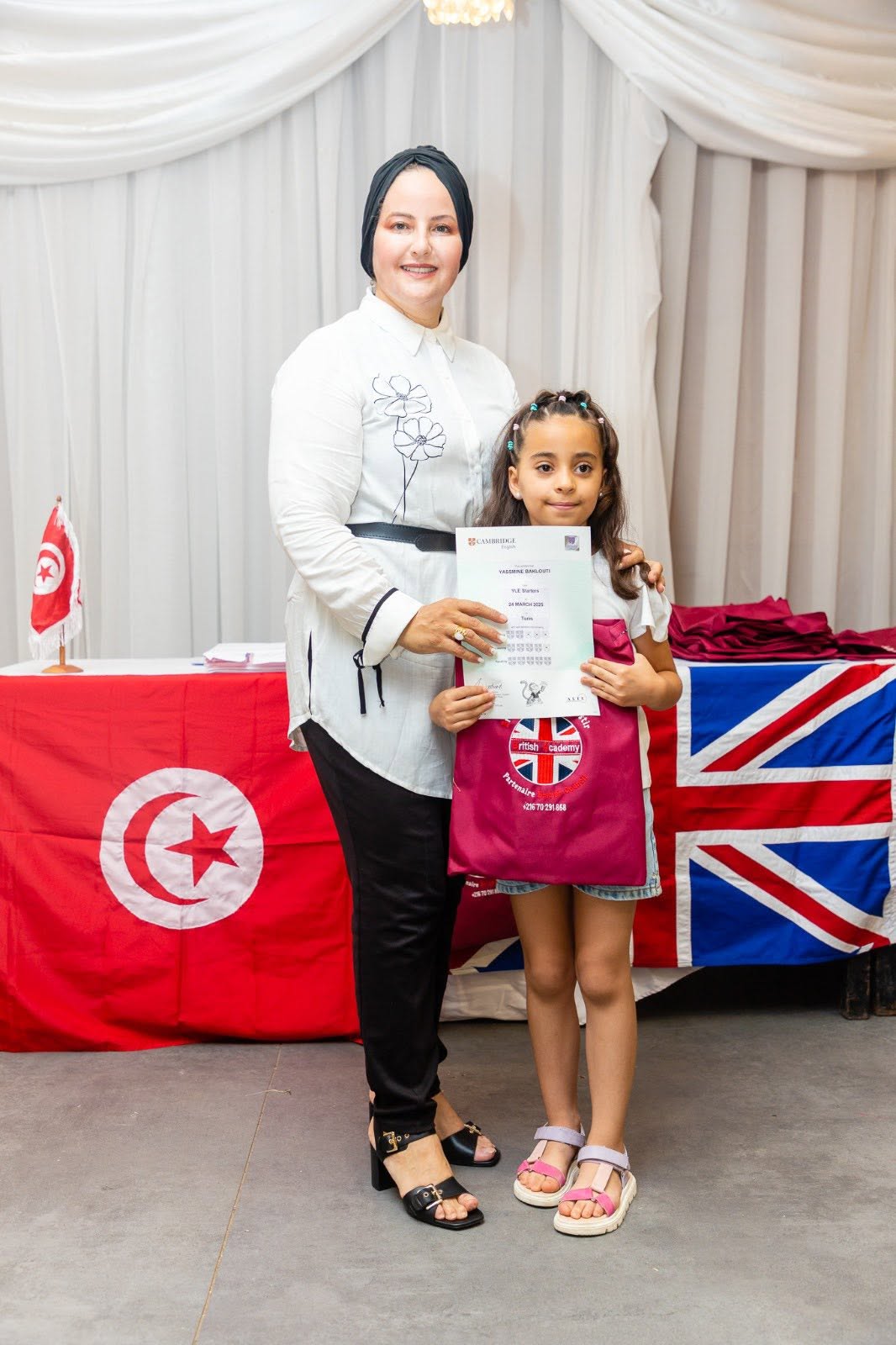 Young student holding her Cambridge English YLE certificate with her teacher