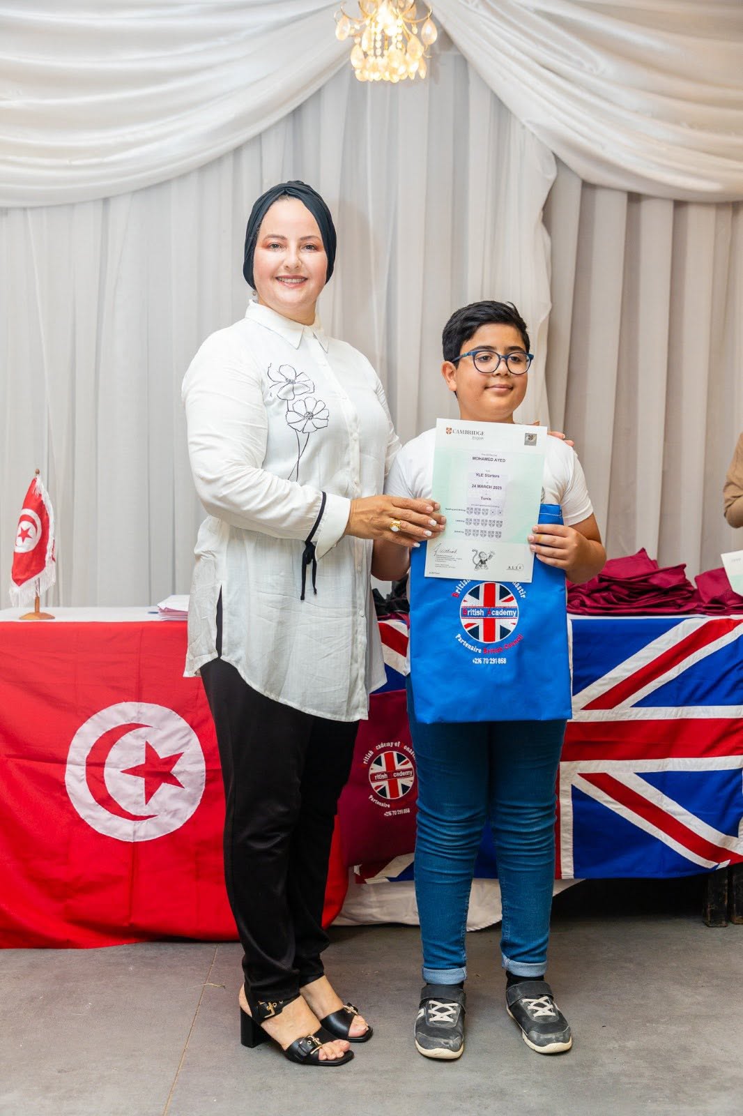 Student holding his Cambridge English YLE certificate with his teacher