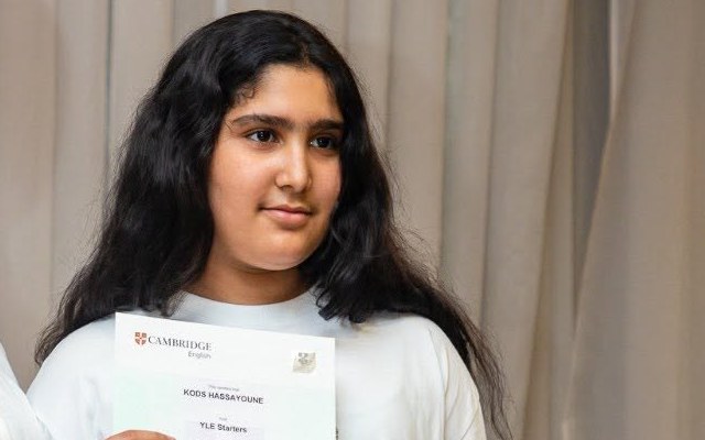 Teen student smiling while holding her Cambridge English certificate